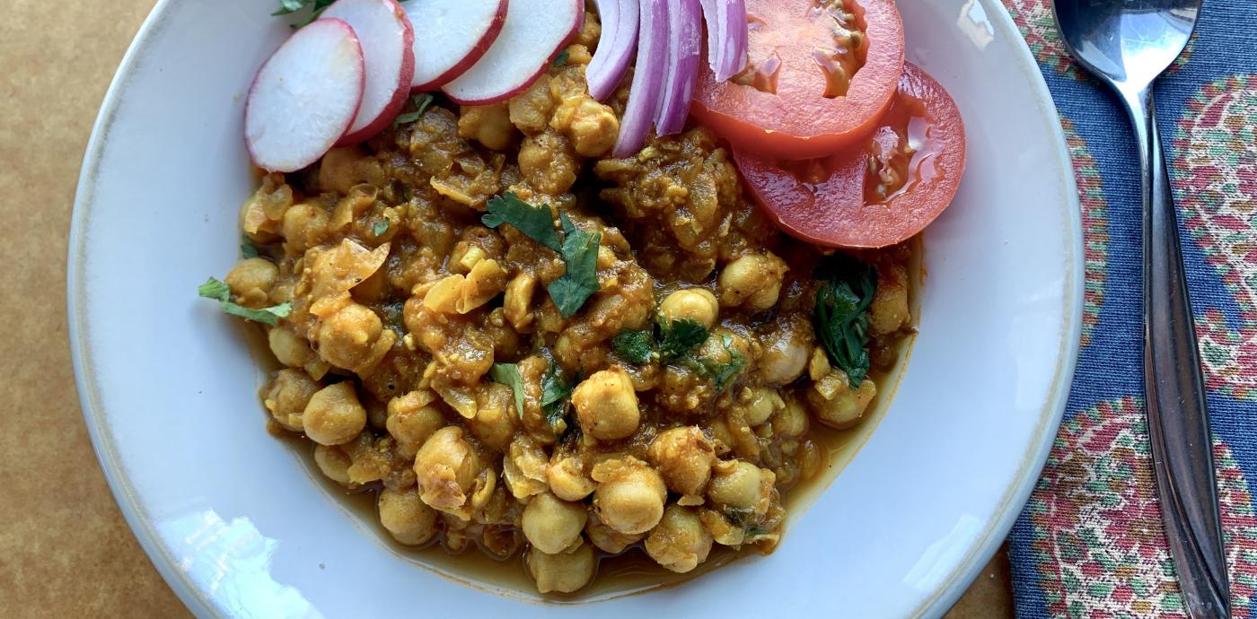 cooked spiced chickpeas in a white bowl, garnished with vegetables
