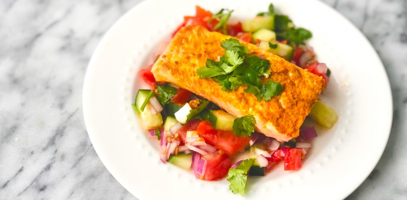 salmon atop a bed of cucumber tomato salad on a white dish 