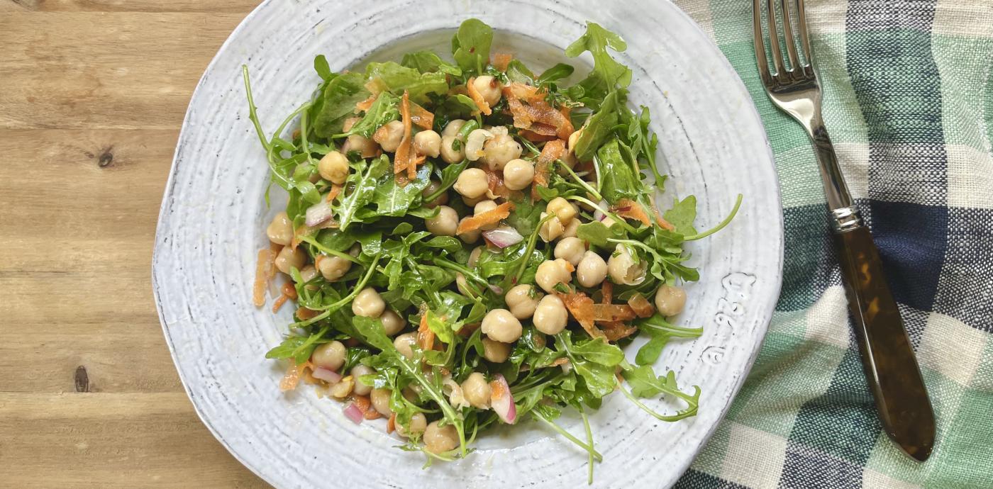 a salad of arugula and chickpeas tossed together in a rustic white shallow bowl