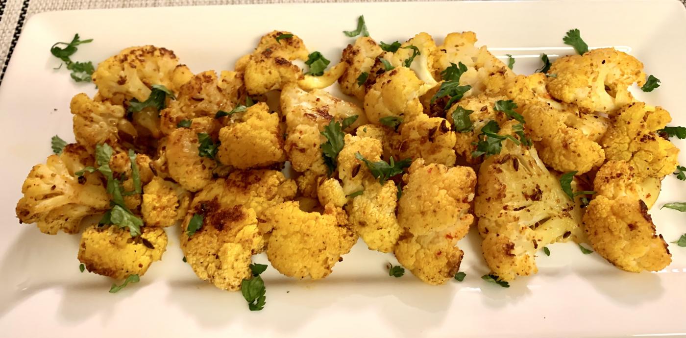 cauliflower florets tinted yellow with spices atop a white platter