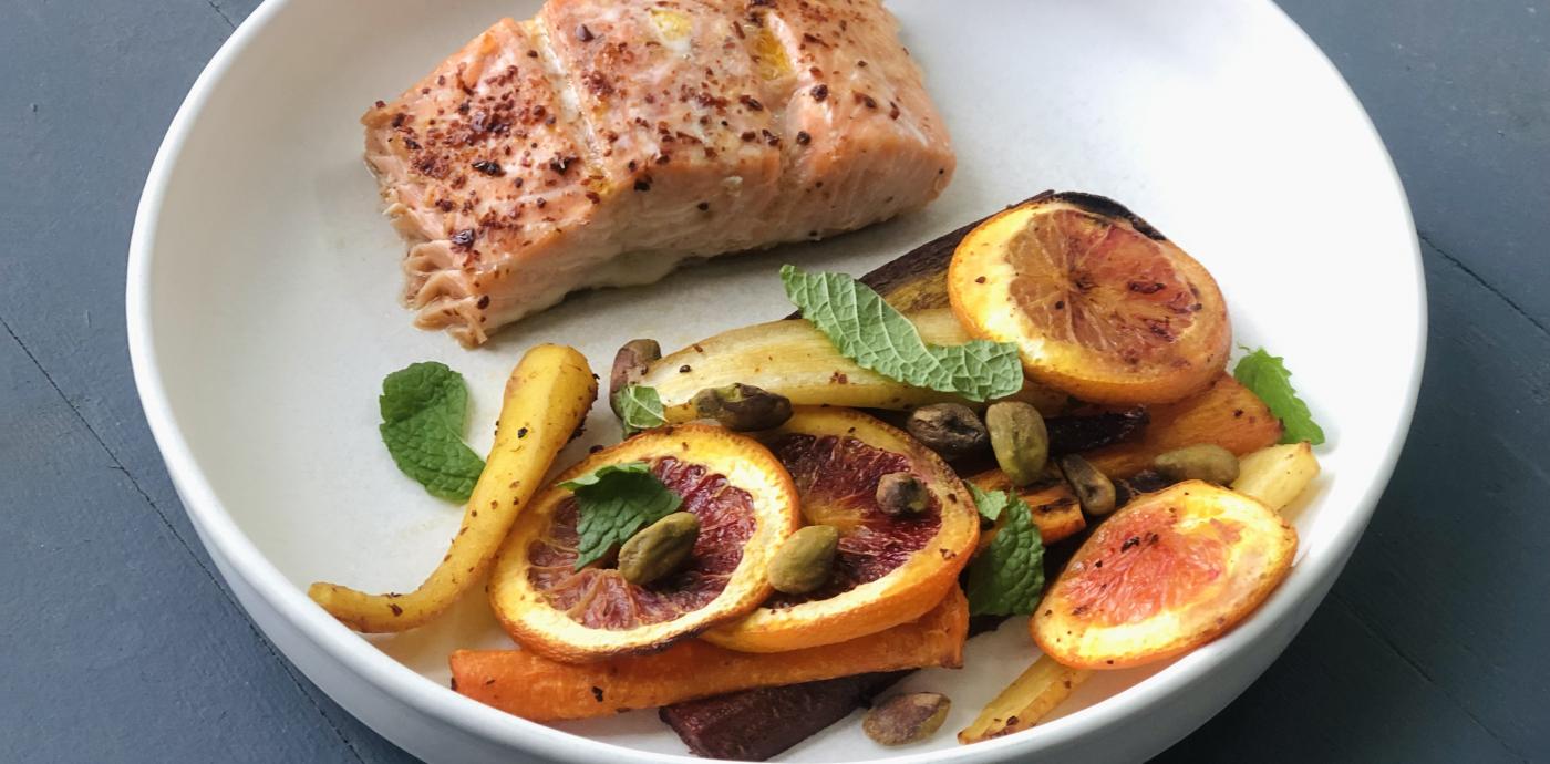 a white shallow dish containing a salmon fillet and a pile of colorful carrots and roasted orange slices