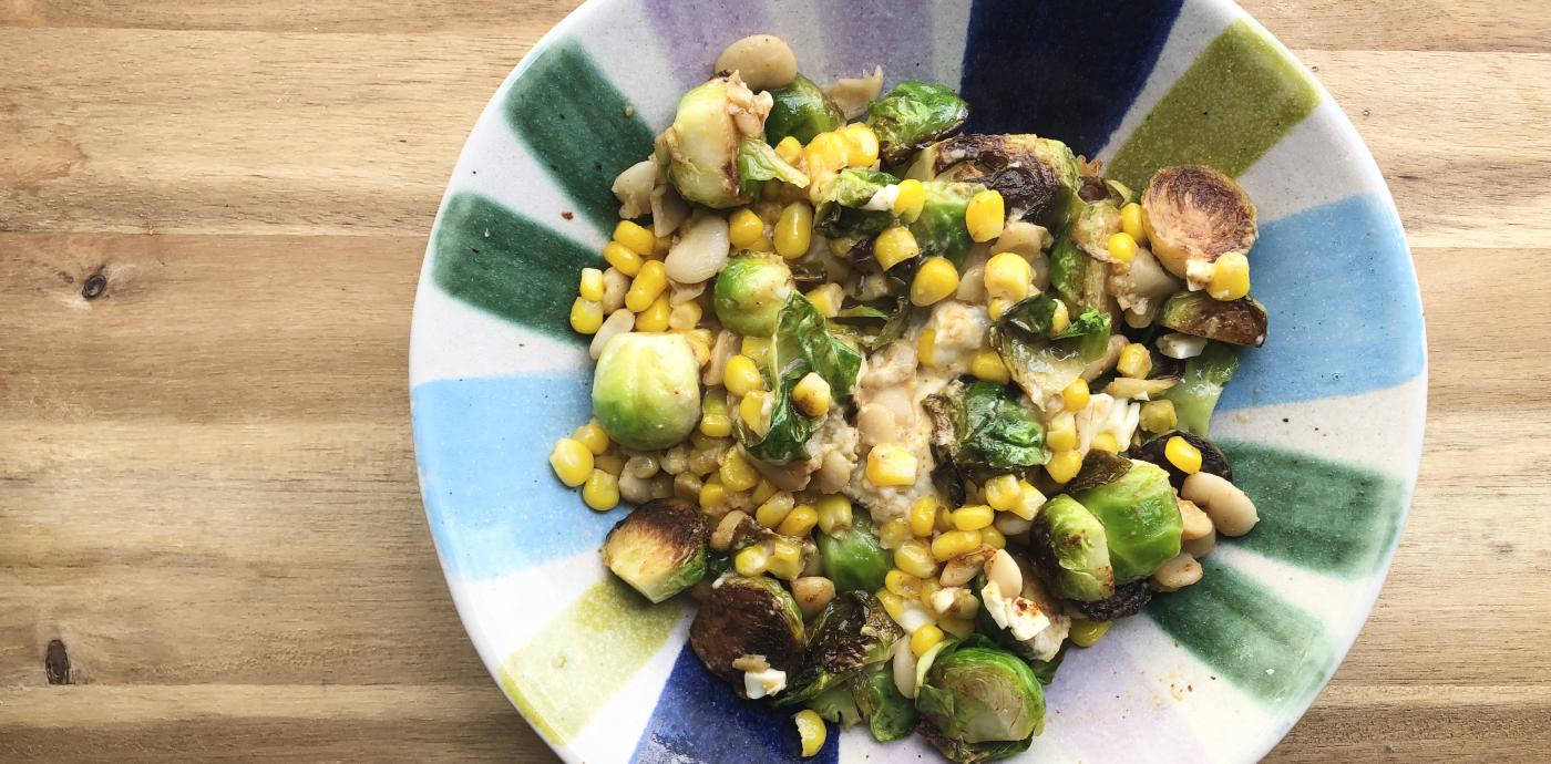 a colorful bowl filled with corn, brussels sprouts, and beans