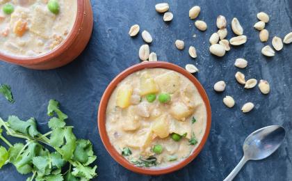 a bowl of creamy soup on a dark backdrop with cilantro and peanuts scattered around