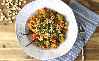 vegetable paella in a rustic white bowl atop a wooden surface with peanuts scattered in the background