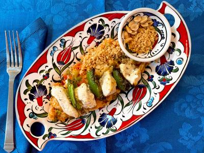 skewer threaded with alternating pieces of grilled chicken and green bell peppers, atop a bed of bulgur on a colorful platter