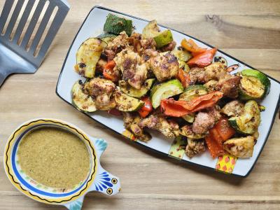chicken and vegetables on a colorful platter with a dish of sauce next to the platter