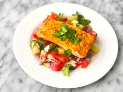 salmon atop a bed of cucumber tomato salad on a white dish 