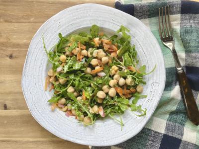 a salad of arugula and chickpeas tossed together in a rustic white shallow bowl