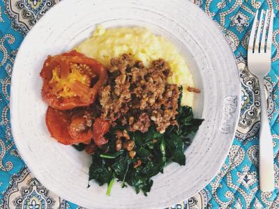 bowl on a placemat with polenta, roasted tomatoes, greens, and chorizo