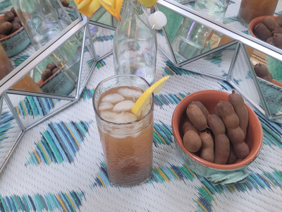a glass filled with a tea-colored liquid and tamarind pods