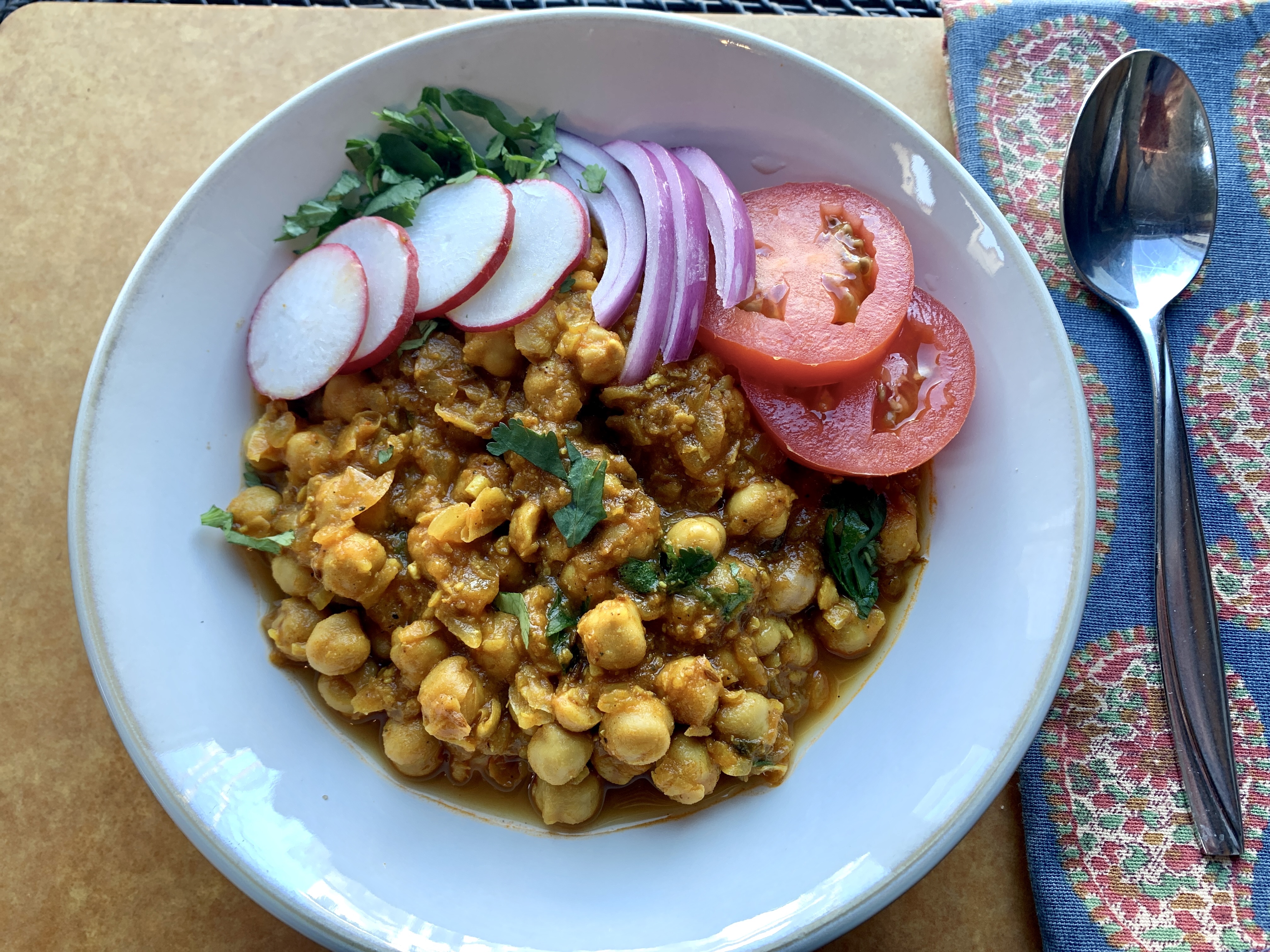 cooked spiced chickpeas in a white bowl, garnished with vegetables