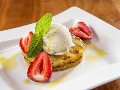 Two slices of grilled pineapple with strawberries, mint and a scoop of ice cream