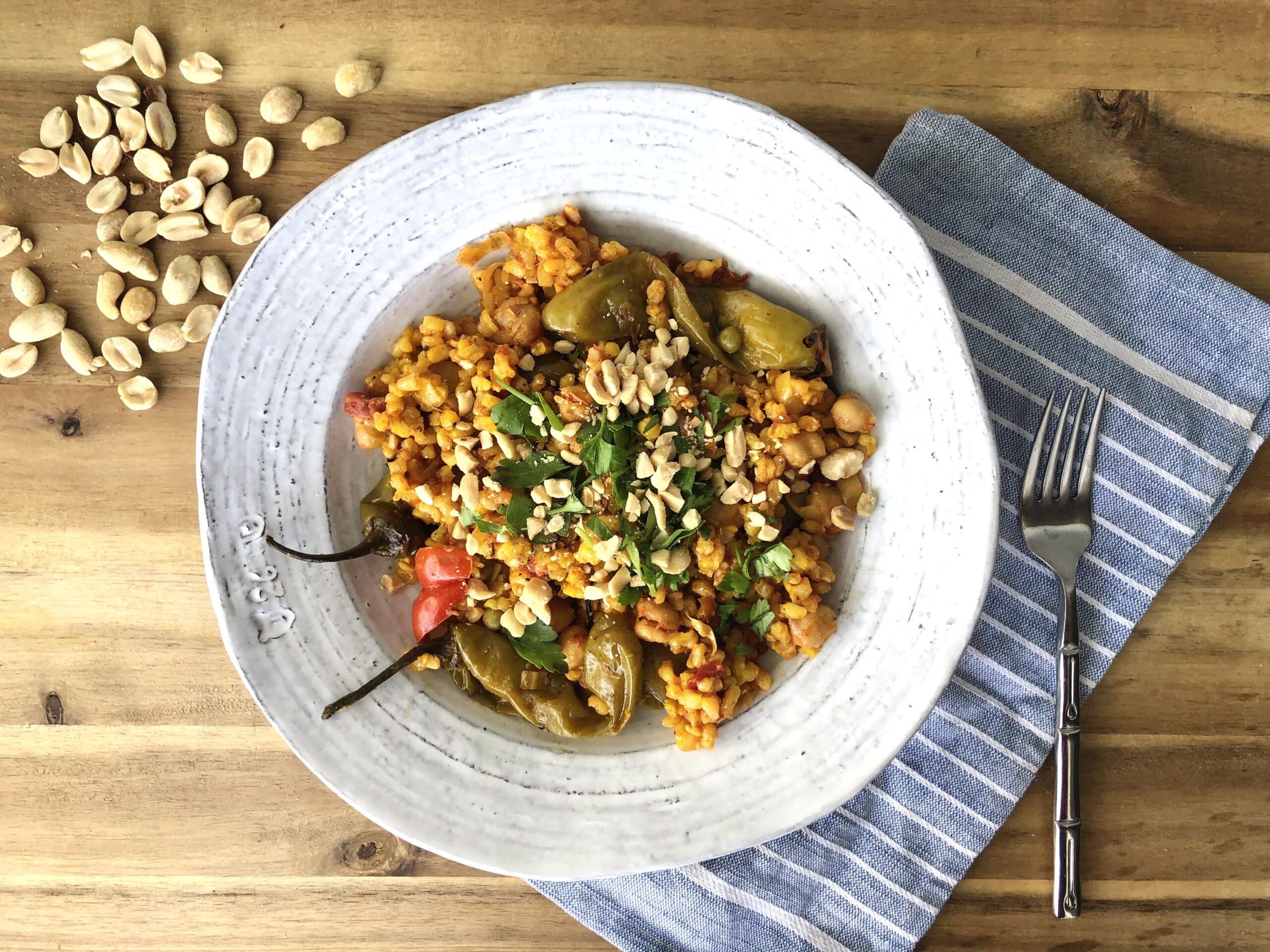 vegetable paella in a rustic white bowl atop a wooden surface with peanuts scattered in the background