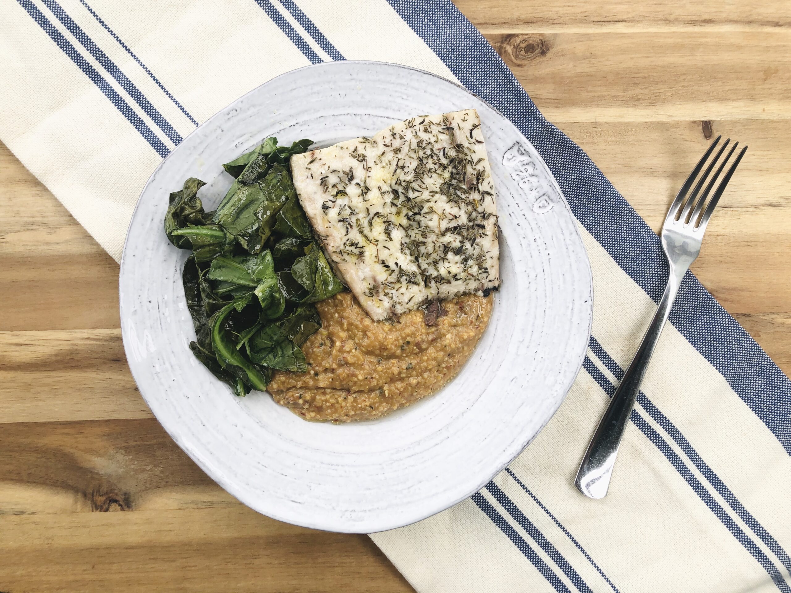 bowl of polenta on a table topped with fish and greens