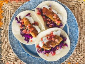 A blue plate featuring three tacos garnished with fresh cabbage and creamy sour cream.