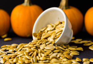 A close-up of pumpkin seeds in a bowl, surrounded by decorative pumpkins, highlighting autumn's harvest.