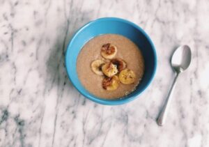 A bowl of banana oatmeal made with coconut milk, garnished with sliced bananas and a sprinkle of coconut flakes.