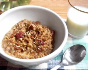 A bowl of oatmeal accompanied by a glass of milk and a spoon