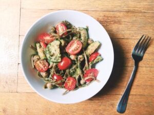 A bowl of pasta topped with fresh tomatoes and green beans, showcasing a vibrant and appetizing meal.