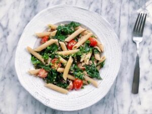 A white plate filled with pasta garnished with fresh tomatoes