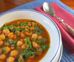 A bowl of soup featuring chickpeas, carrots, and spinach, showcasing a vibrant and nutritious meal.