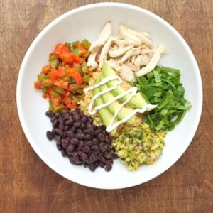 A colorful bowl containing beans, rice, black beans, avocado, and various fresh ingredients, showcasing a nutritious meal.