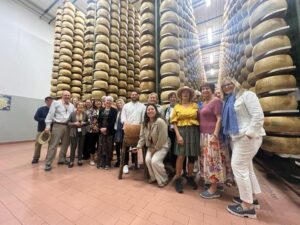 A group of people smiles while standing in front of a large wheel of cheese at a food festival.