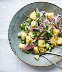A plate of fresh cucumber, onion, and potato salad garnished with herbs, showcasing vibrant colors and textures.
