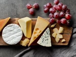 A wooden cutting board displays an assortment of cheese and fresh grapes arranged artfully.