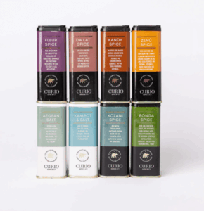 Curio Spice products arranged in two rows of four, showcasing various spices and salts with distinct labels.