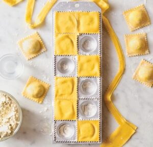 Ravioli dough with filling molds on a marble countertop.
