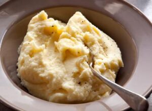 A bowl of creamy mashed potatoes with a silver spoon resting on the side
