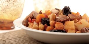 A wooden table displays a bowl containing a mix of nuts and raisins