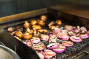 Onions and mushrooms are cooking on a grill