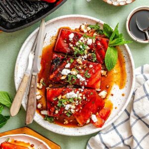 Grilled red peppers topped with crumbled feta cheese and fresh mint leaves on a white plate