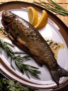 Grilled fish on a white platter garnished with herbs and lemon slices