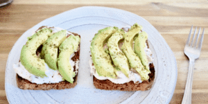 Two slices of whole grain toast with creamy spread, topped with avocado slices