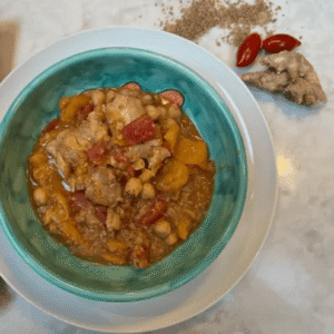 A bowl of colorful vegetable stew with spices on a clean white table