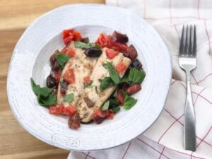 A plate featuring grilled chicken, fresh tomatoes, and vibrant basil leaves.