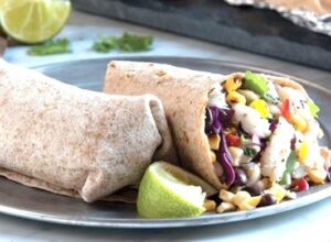 Two whole wheat burritos on a plate with lime and filling visible