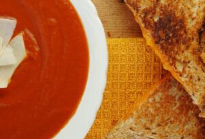A warm grilled cheese sandwich served with a steaming bowl of tomato soup